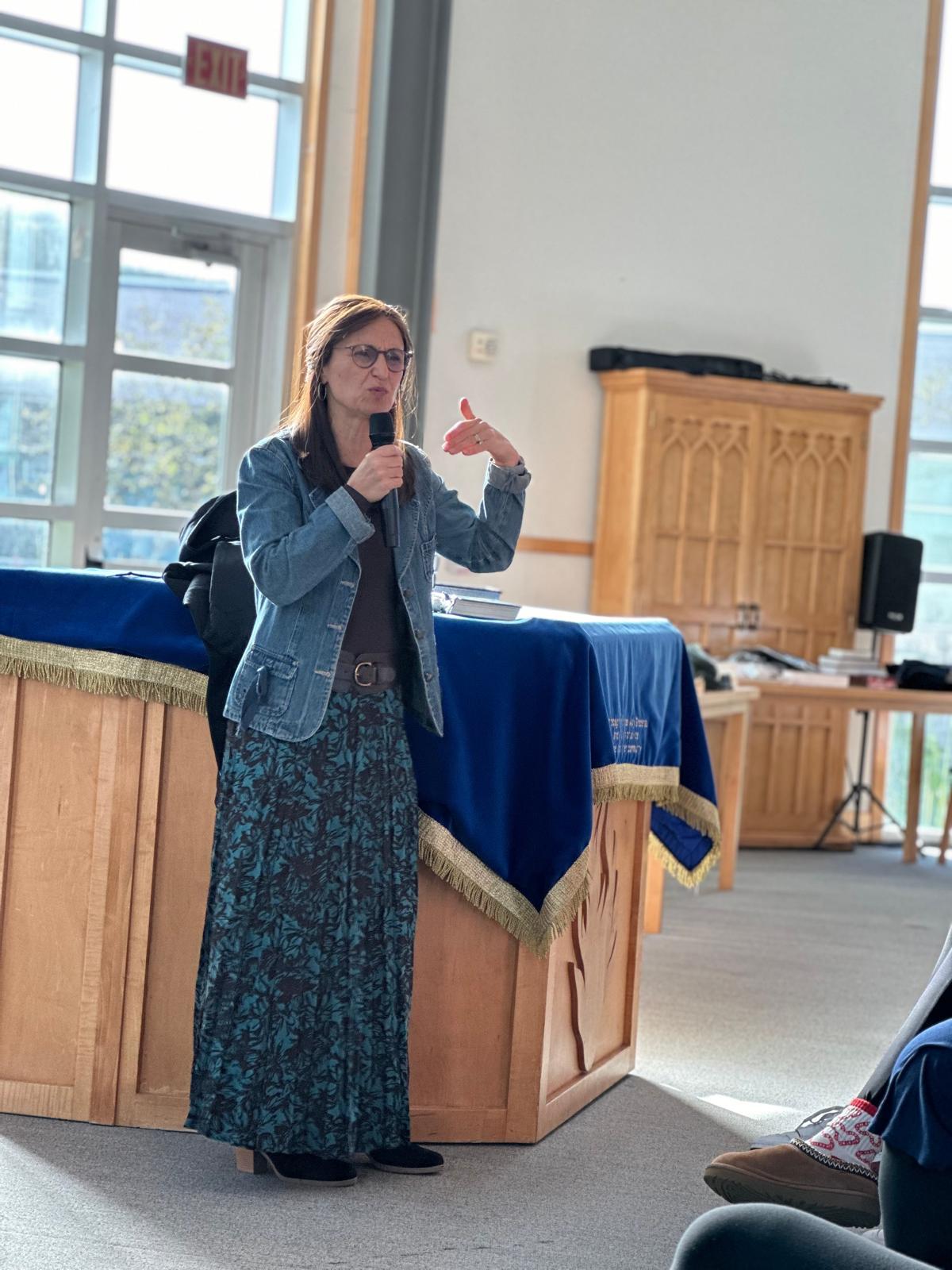 Jen speaking with a microphone in a synagogue sanctuary